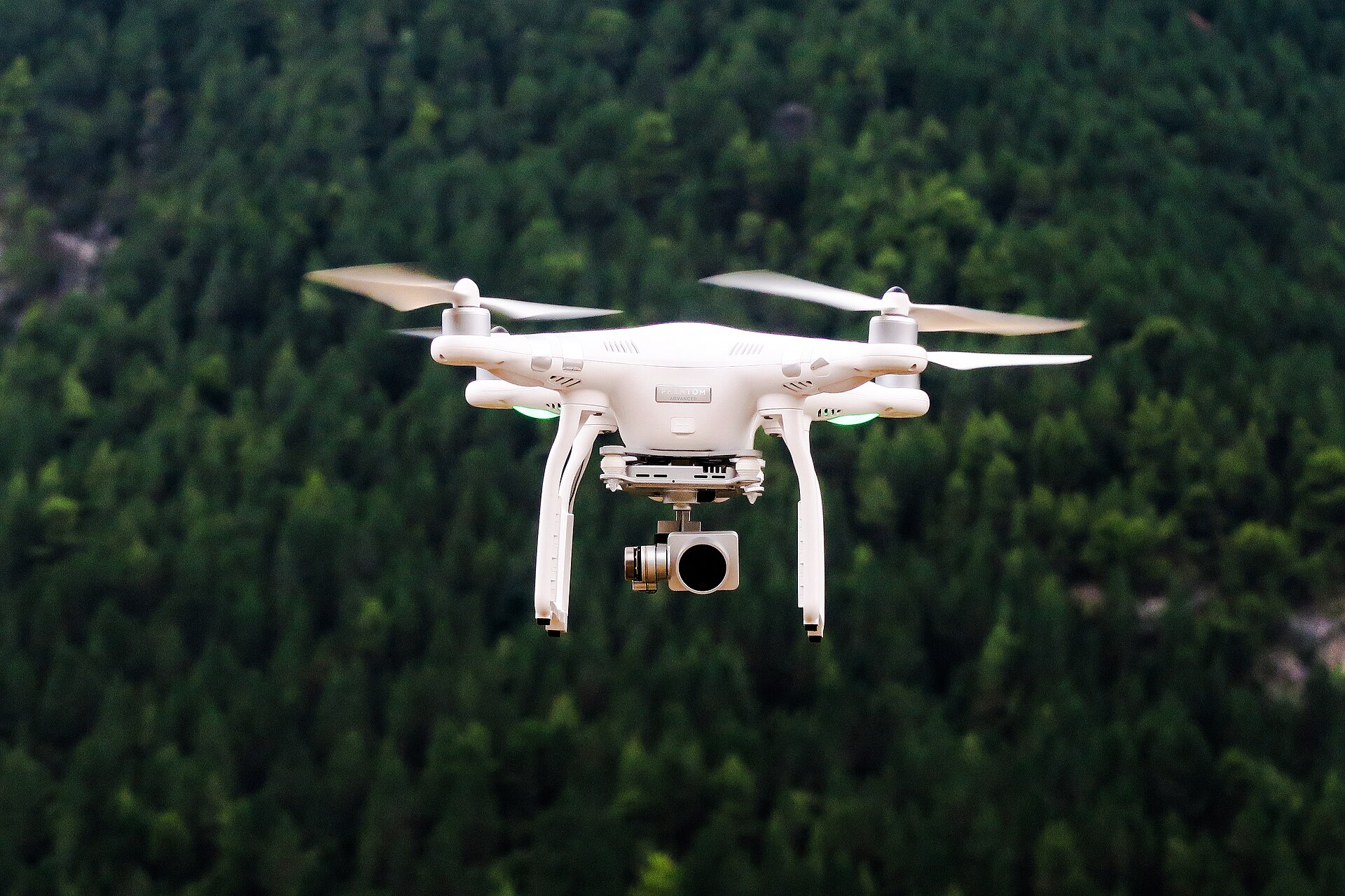 A camera drone hovering above a dense green forest canopy